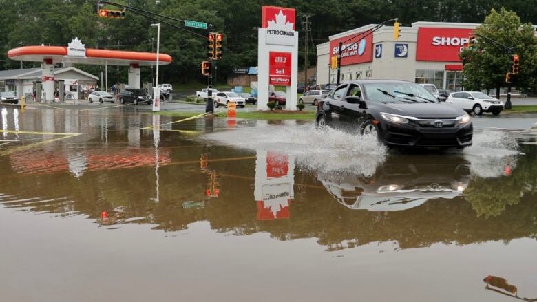 A car drives through a flooded road by a gas station.