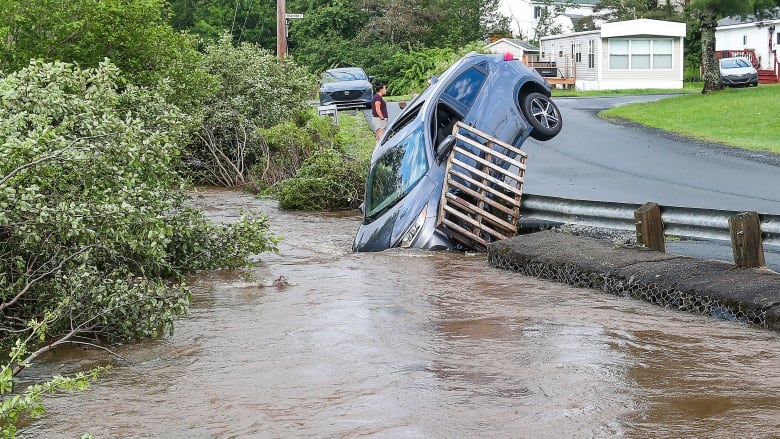 A car is seen stuck on a guardrail at the edge of floodwaters in Middle Sackville, N.S., in July.