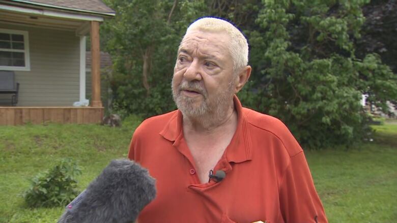 A man in a burn sienna t-shirt speaks into a microphone. 