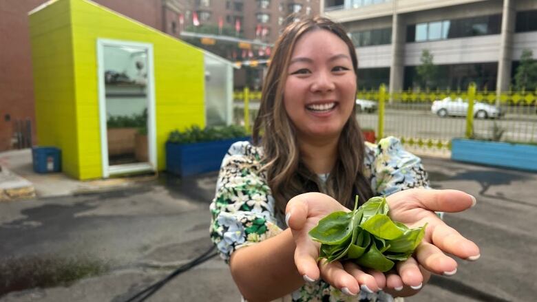 A woman holds out two palmfuls of basil. 