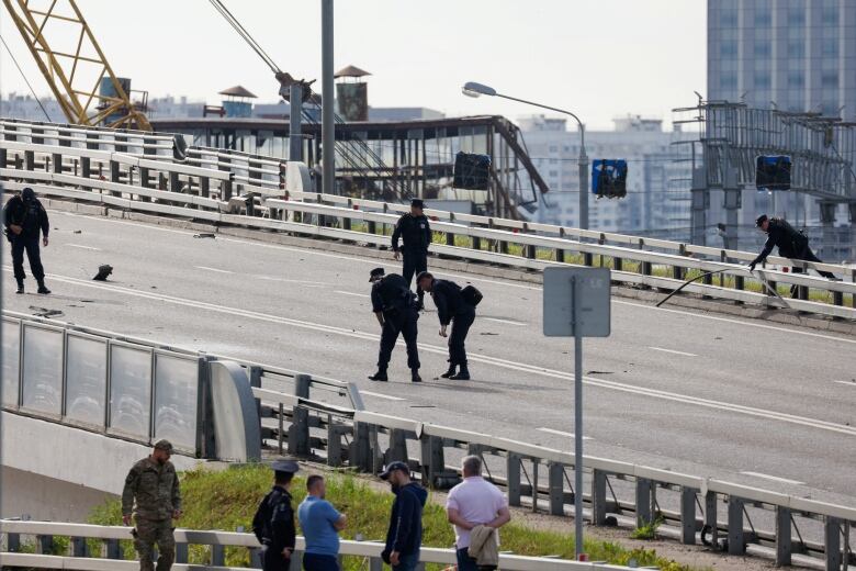 Men in black uniforms examine debris on an urban highway overpass 