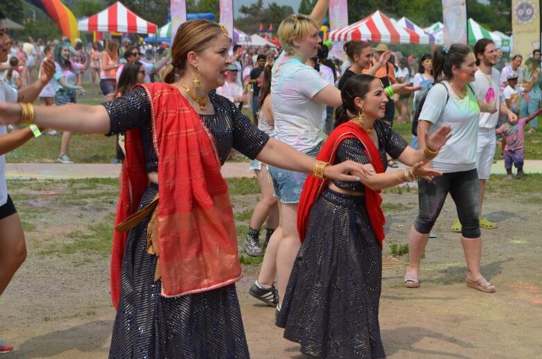 Two women wearing Indian sarees dance at the Festival of India. They are wearing matching black sarees with a red drape.