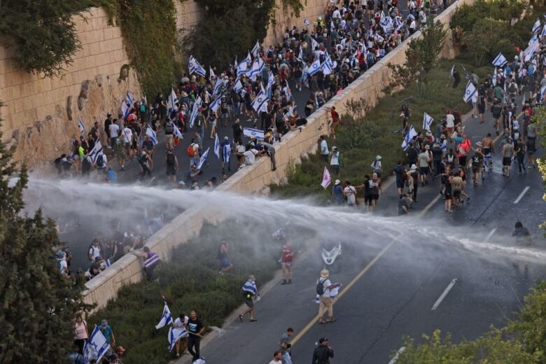 Water cannons are fired at protesters across a highway.