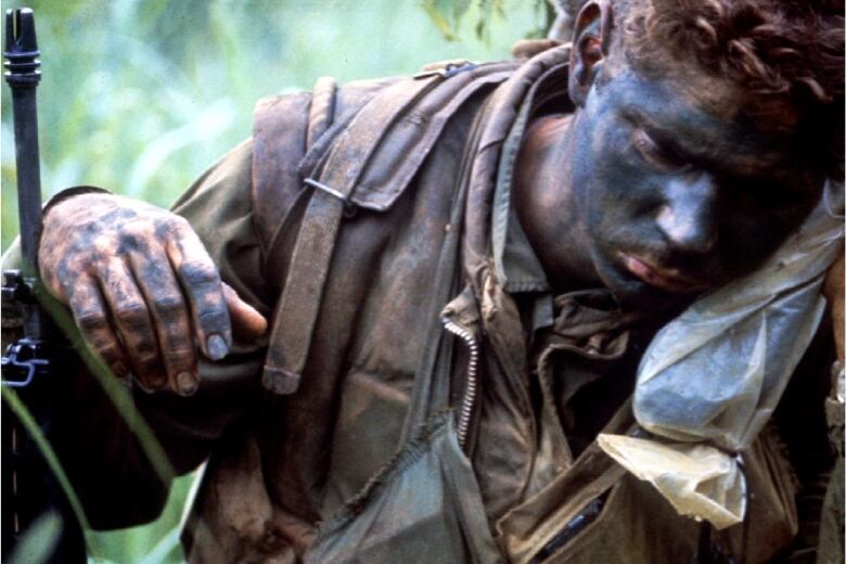 Soldier in military fatigues with face covered in black grime.