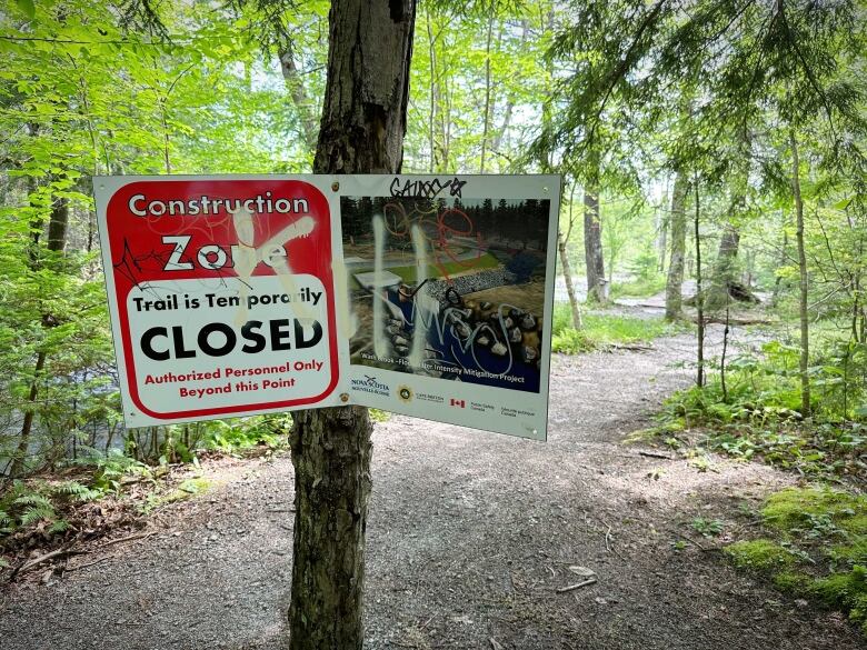 A sign is seen attached to a tree noting that part of the traisl through the forest are closed due to construction of flood controls.