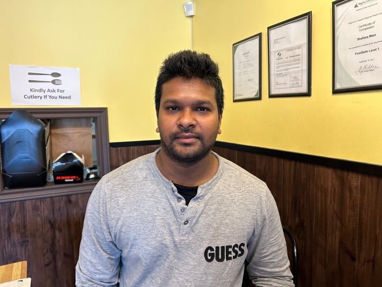 A man in a grey shirt stands against a yellow wall.