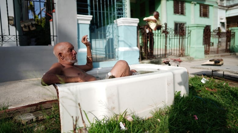 An elderly man lies in a bathtub on a public street.