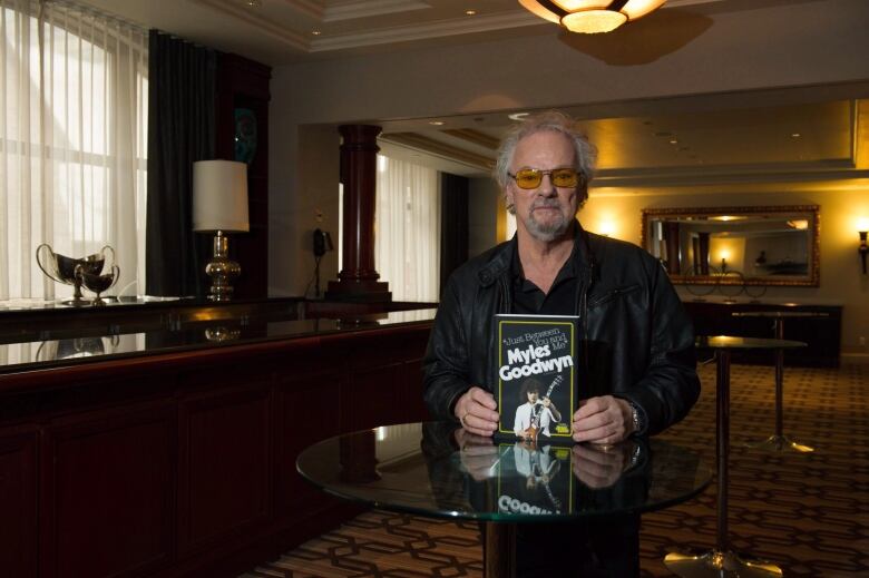 A man holding a book he wrote poses for the camera.