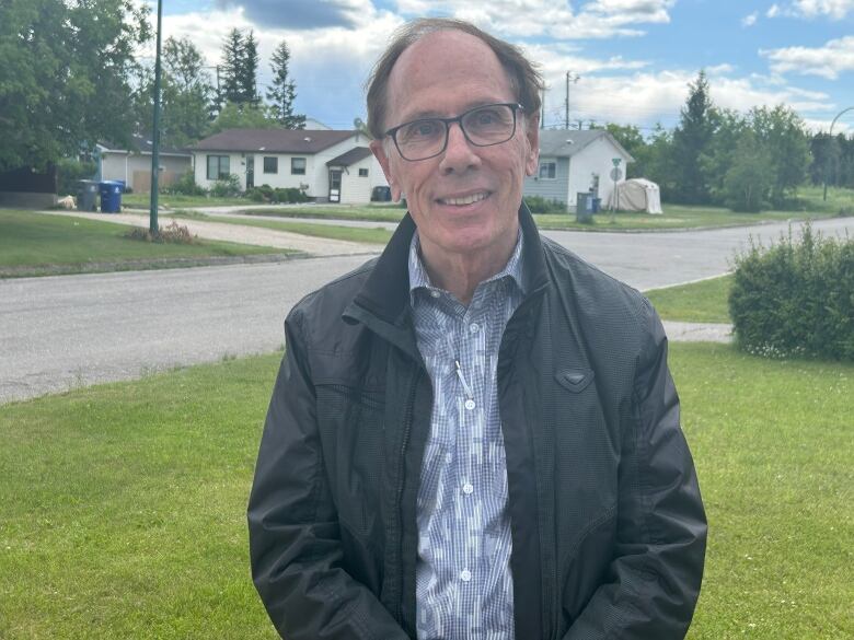 A man in a black jacket and a button up shirt standing on the road. 