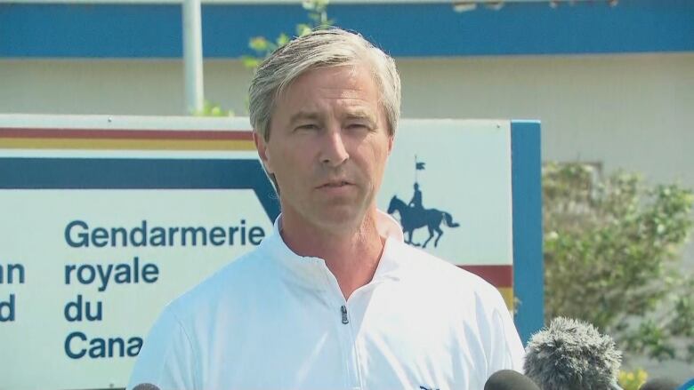 A man wearing a white shirt stands in front of an RCMP sign.