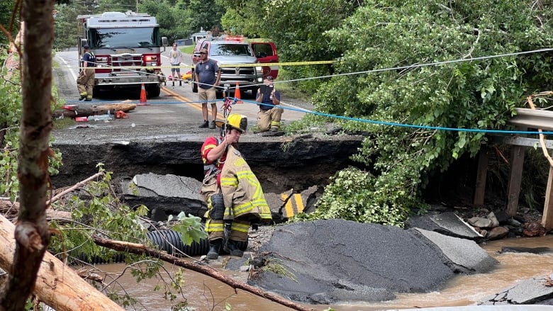 A firefighter dangles over a washed out road on a highline wire. Road debris is seen in the muddy waters below.