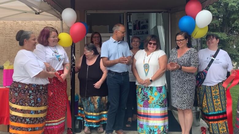 A group of people, cut a red ribbon at the front of an apartment building.