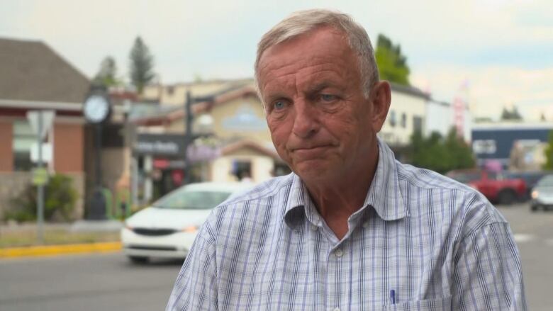 A man with white hair and a blue checked shirt stands on a downtown street on a smoky day.