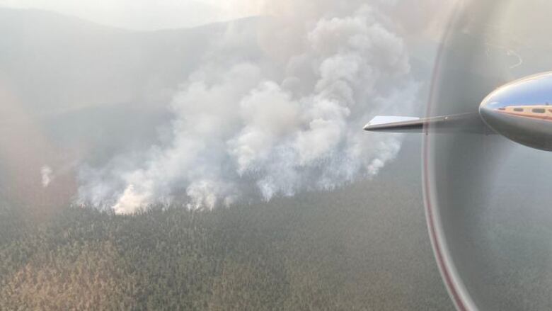 A wildfire is seen from the air, with a plane wing in the frame.