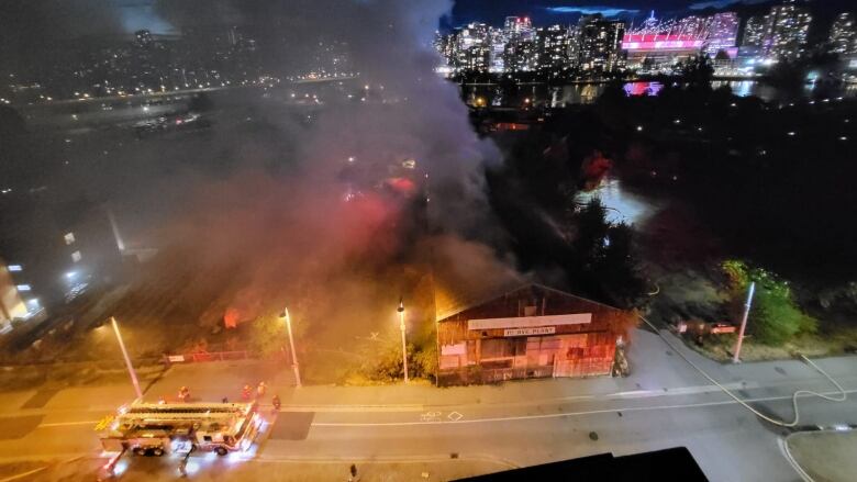 Flames emerge from a building that looks like a barn, across the water from downtown Vancouver.