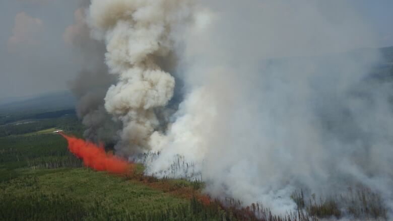 An aerial photo of a firefighting plane dropping red fire retardant on an area of forest shrouded in smoke.