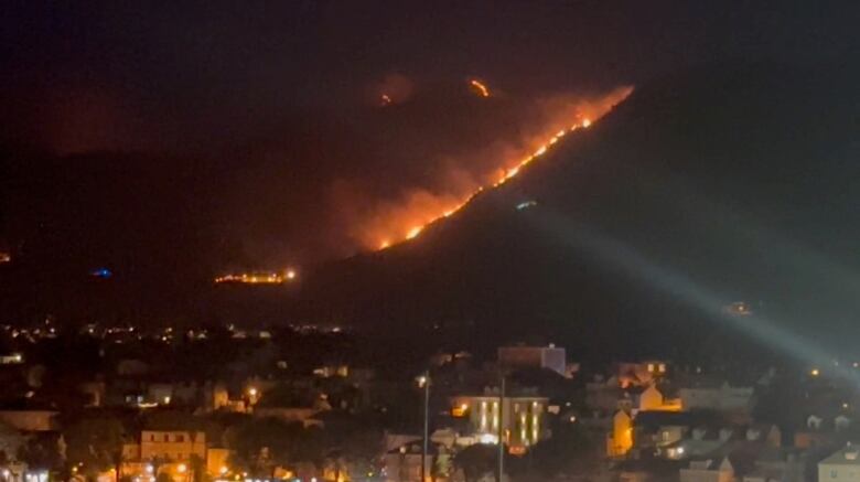 A line of fire can be seen running up a hillside above a community at night.