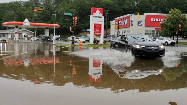 A car drives through a flooded road by a gas station.