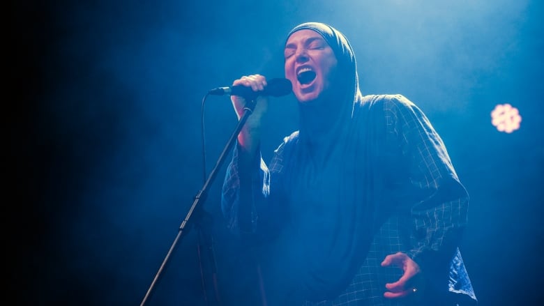 A singer in headscarf sings in front of a mic on stage.