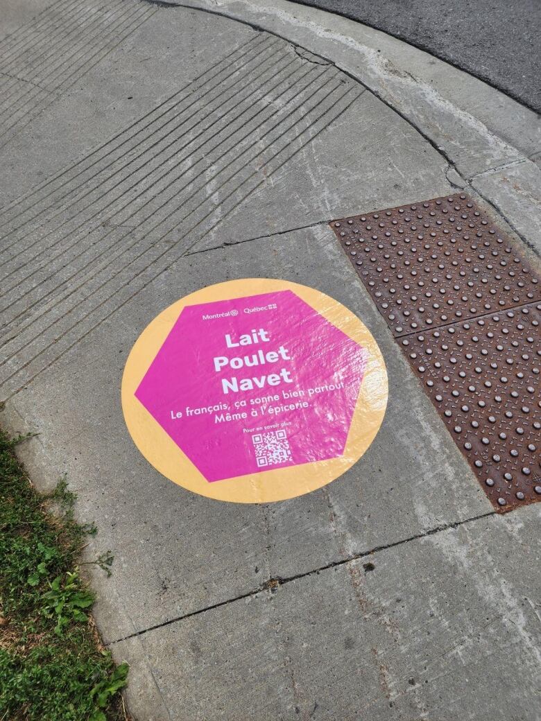 A circular, yellow sticker with pink hexagon and white text is pasted on a sidewalk.