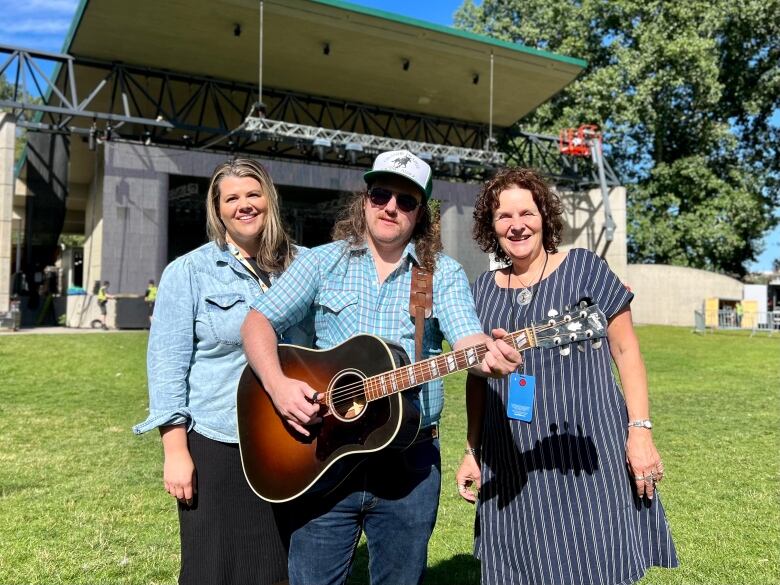 A performer in a guitar is pictured next to two women as they smile at the camera.