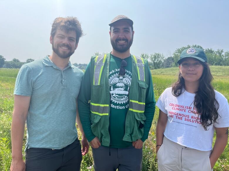 Three young people stand in front of a marshy bay