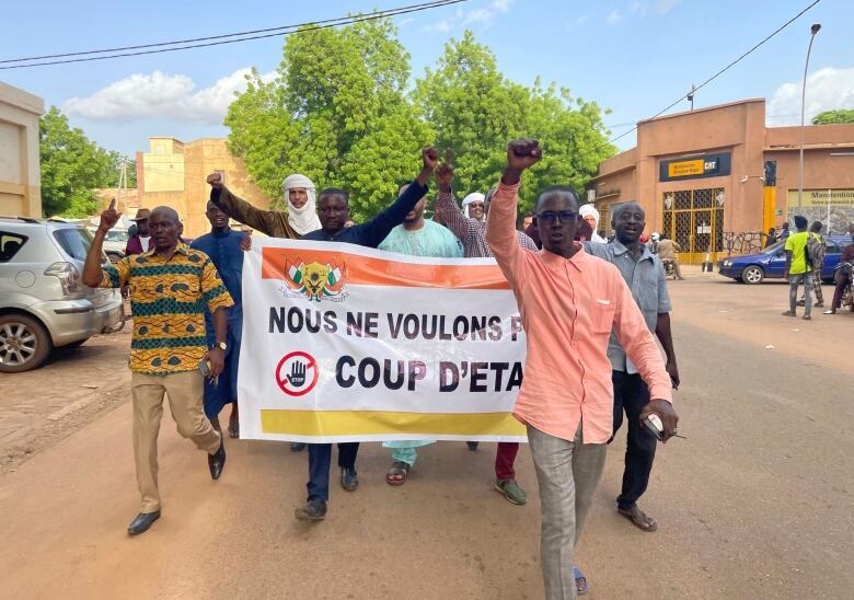 Several men are shown walking down a street while holding up a banner.