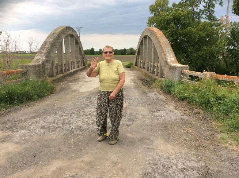 A woman stands on a gravel road on a cement bridge.