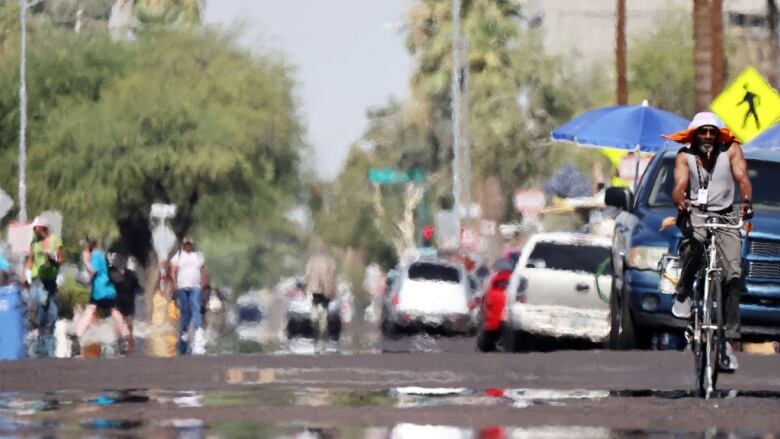 A man, to the right, rides his bicycle during a heat wave.