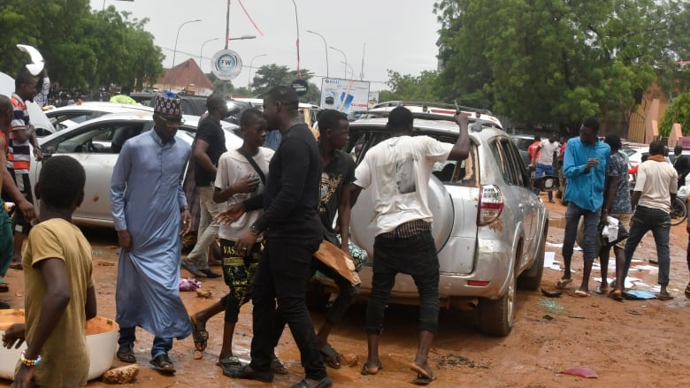 Several men on a muddy street are shown surrounding a vehicle.