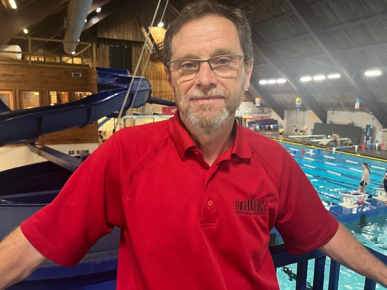 Standing in a red shirt, Craig Neil poses for a picture in front of the diving boards at the Aquarena.