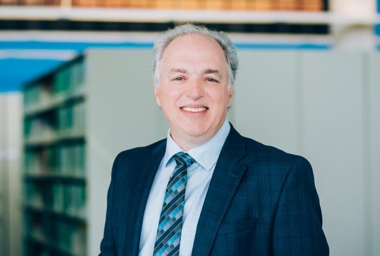  A man in a suit smiles for a photo in a library.