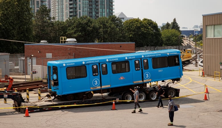 A blue rail car sits on top of a trailer bed inside a transit yard.