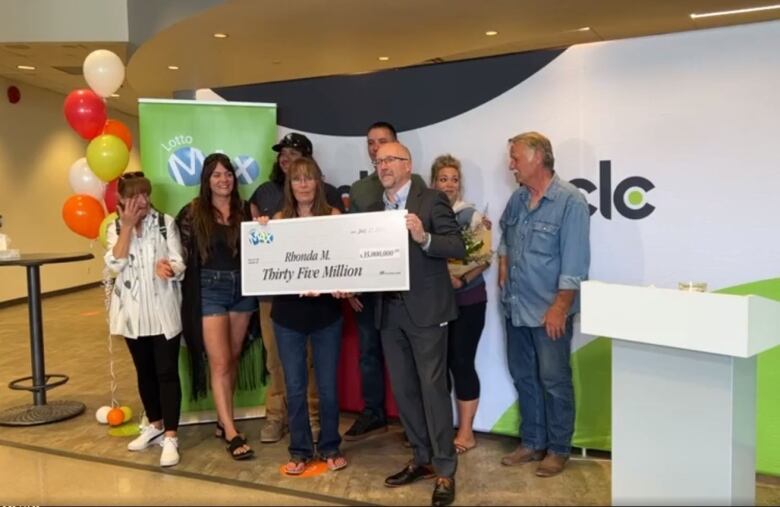 A group of people stand together, holding a big cheque.