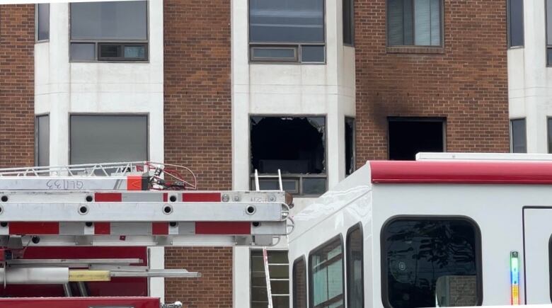 A broken window in a red brick building with a fire truck parked inside. 