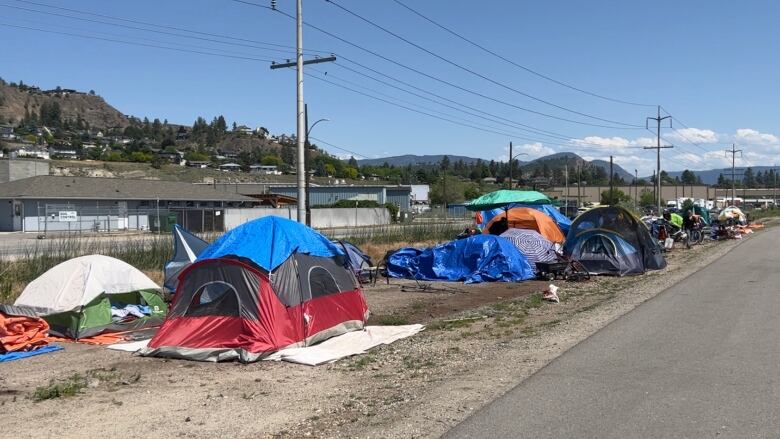 A line of tents situated along a road with utility poles and a hill in the background.