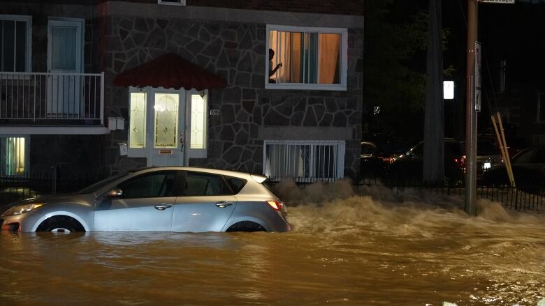 Major flooding partially submerges a car as a resident looks out their window onto the flooded street. 