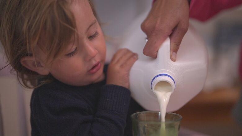 Child poring milk from plastic jug.