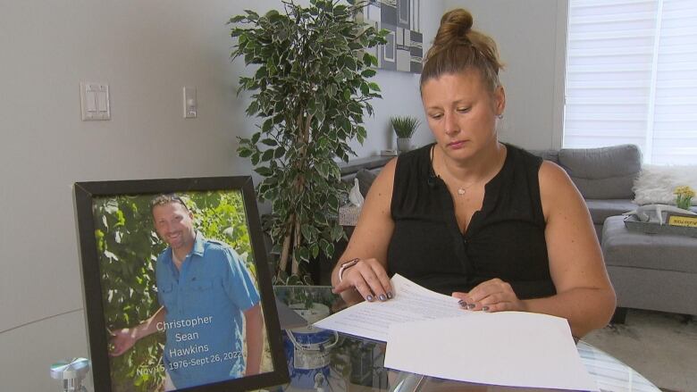 A woman sitting at a table flipping through papers with picture of brother in front of her.