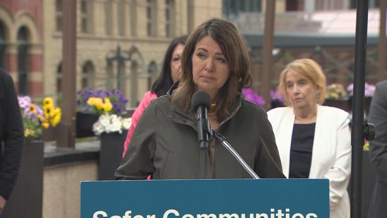 A woman in a green coat speaks into a microphone. 