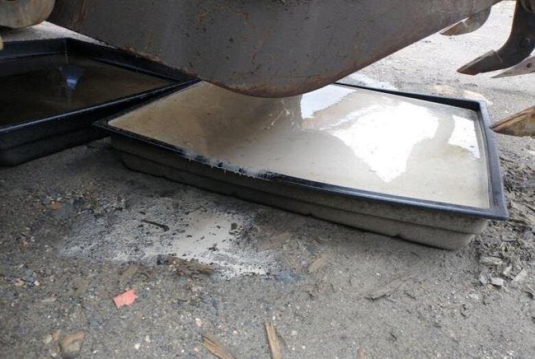 An overflowing spill tray is seen underneath a vehicle.