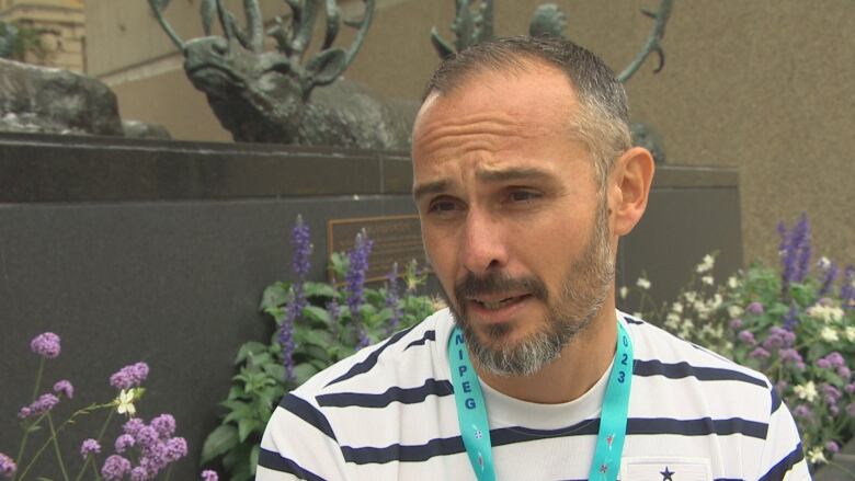 A man in a T-shirt wearing a lanyard around his neck speaks to someone off-camera.