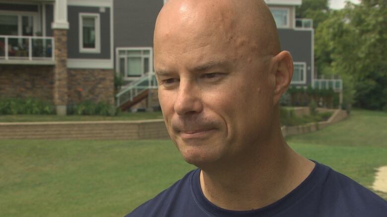 A bald man listens to someone speak outside a large building.