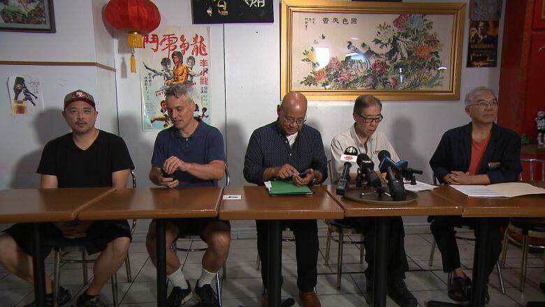 Five men sit at a table before a news conference.