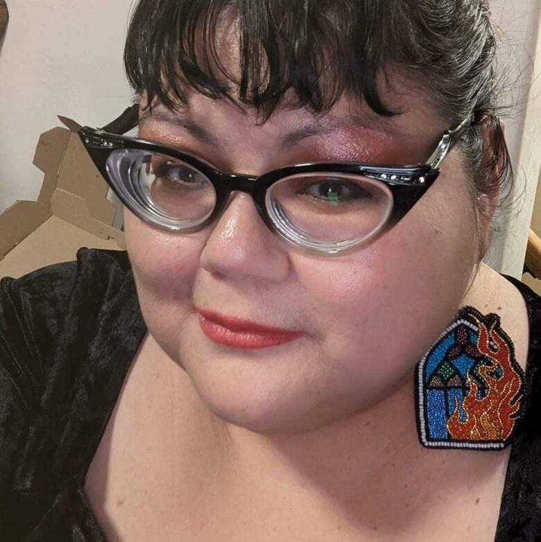 A first nation woman with glasses and beaded earrings looks up into the camera for a picture