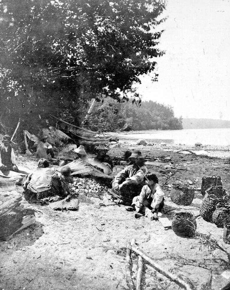 A black and white photo of people sitting on a beach