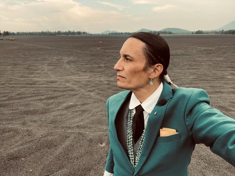 A Dine/Navajo man in a suit stands in a desert landscape.