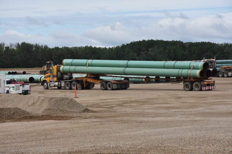  A heavy truck carrying long green pipe sits on a brown gravel surface.