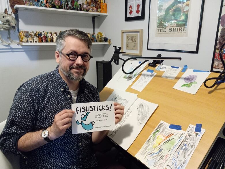 Man holding up comic book in front of artist desk.