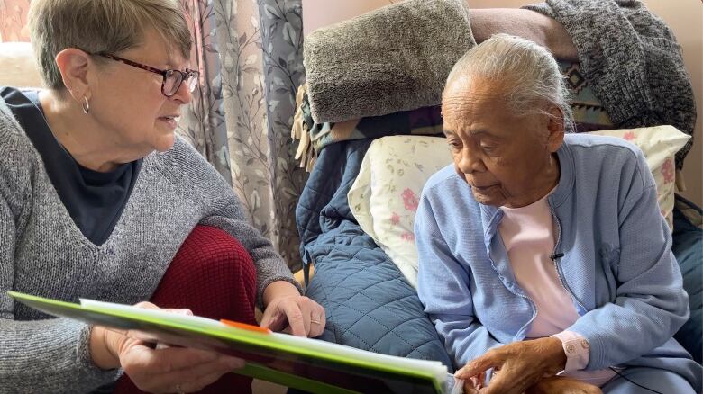 An elderly woman and a younger woman look at photos.